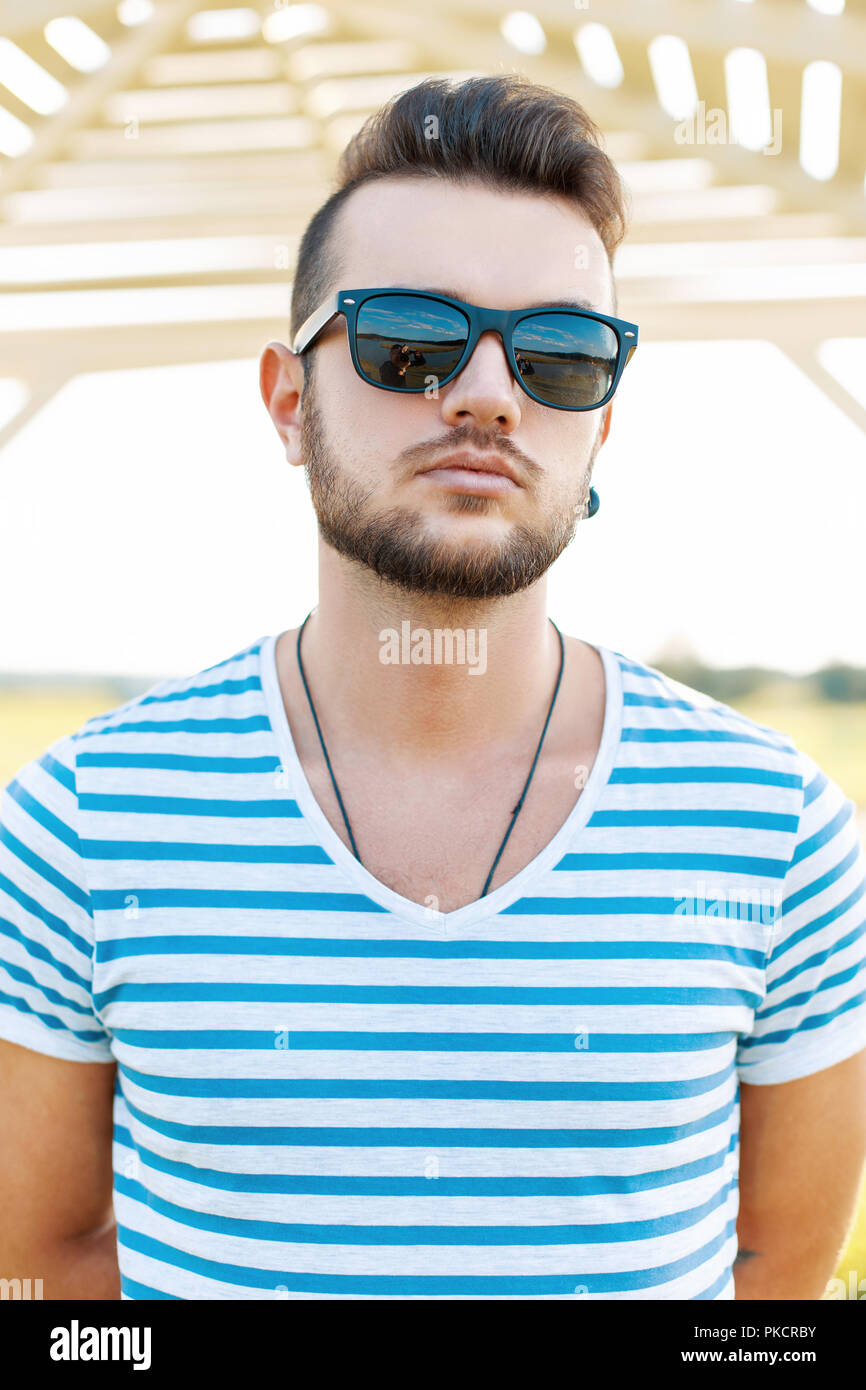Handsome man in a t-shirt with the beard in sunglasses standing on the beach. Stock Photo