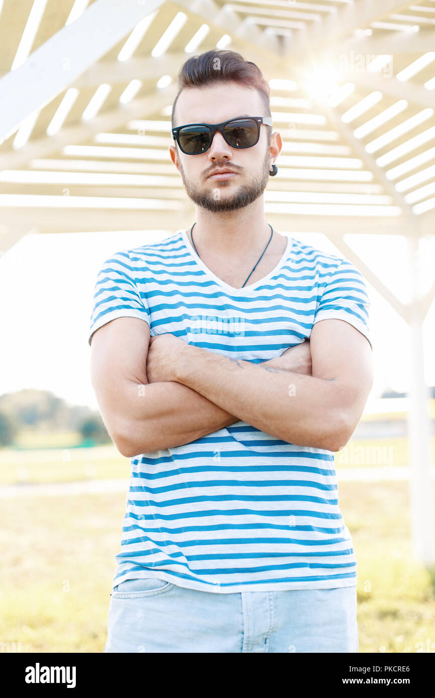 Handsome man with a beard in a summer shirt and sunglasses standing on the beach on a sunny day. Stock Photo