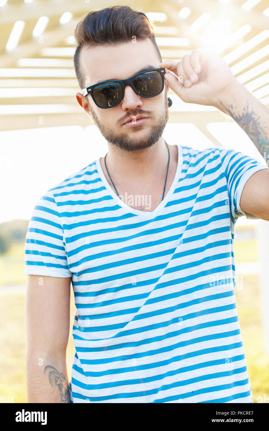 Handsome man in a stylish summer shirt corrects Sunglasses on the beach. Stock Photo