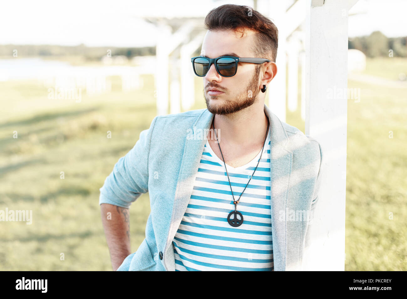 Handsome hipster man in sunglasses with a beard in a trendy suit and shirt on the beach. Stock Photo