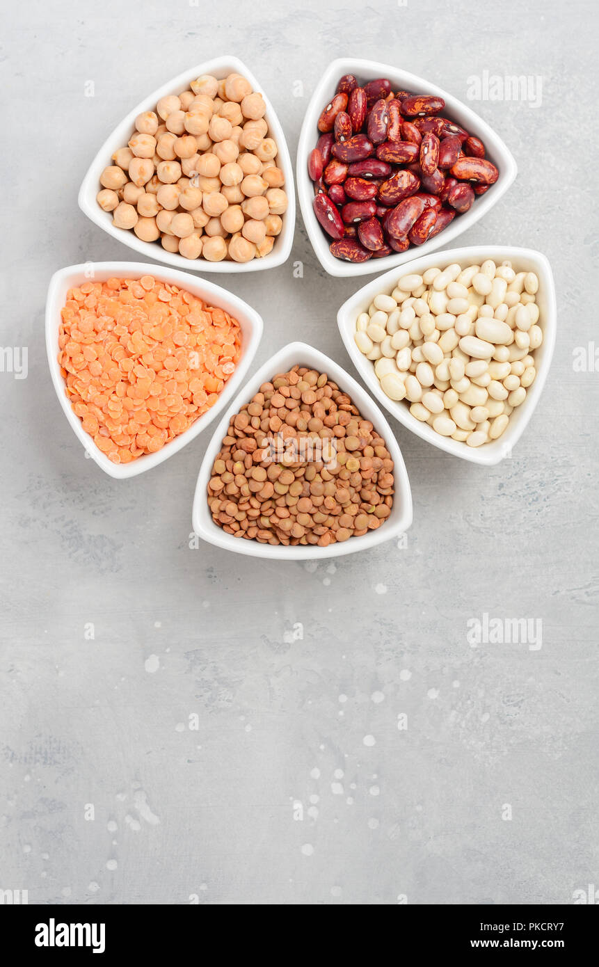 Selection of dry legumes, lentils and peas in white bowls on gray concrete background. Stock Photo