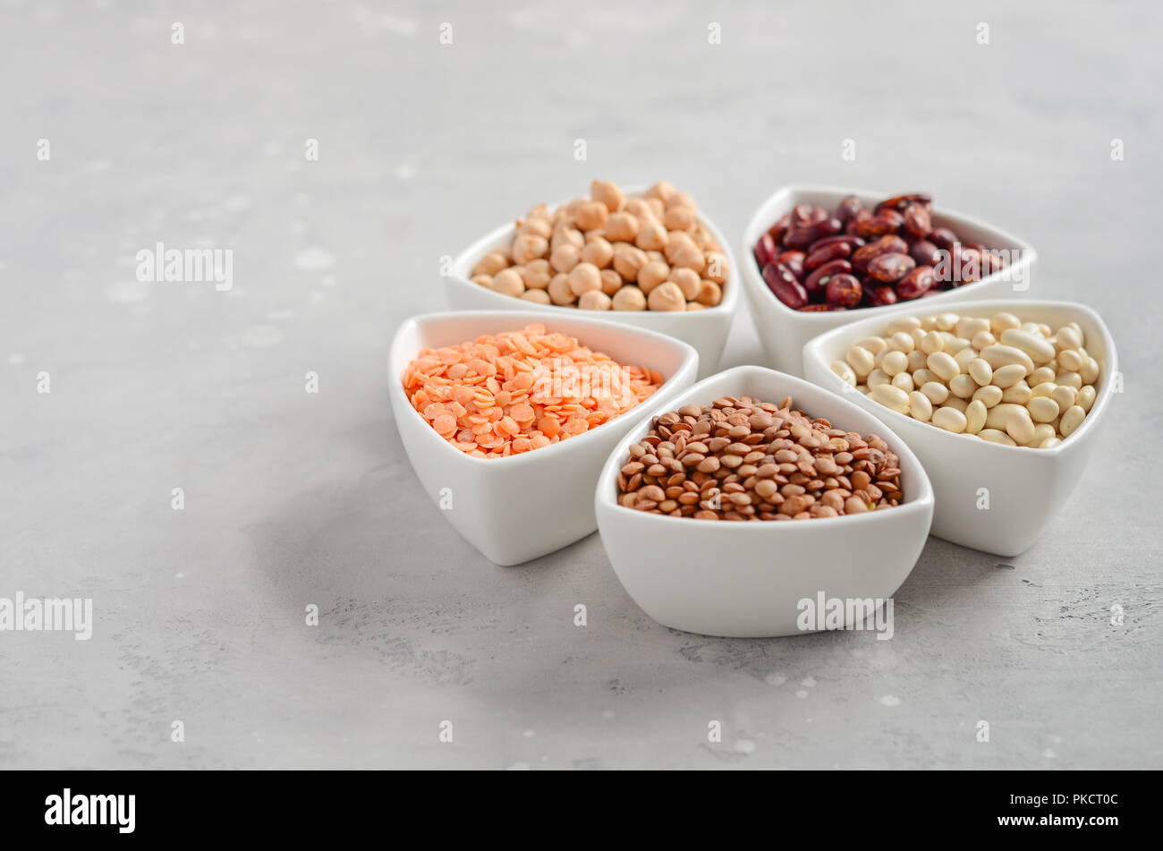 Selection of dry legumes, lentils and peas in white bowls on gray concrete background. Stock Photo
