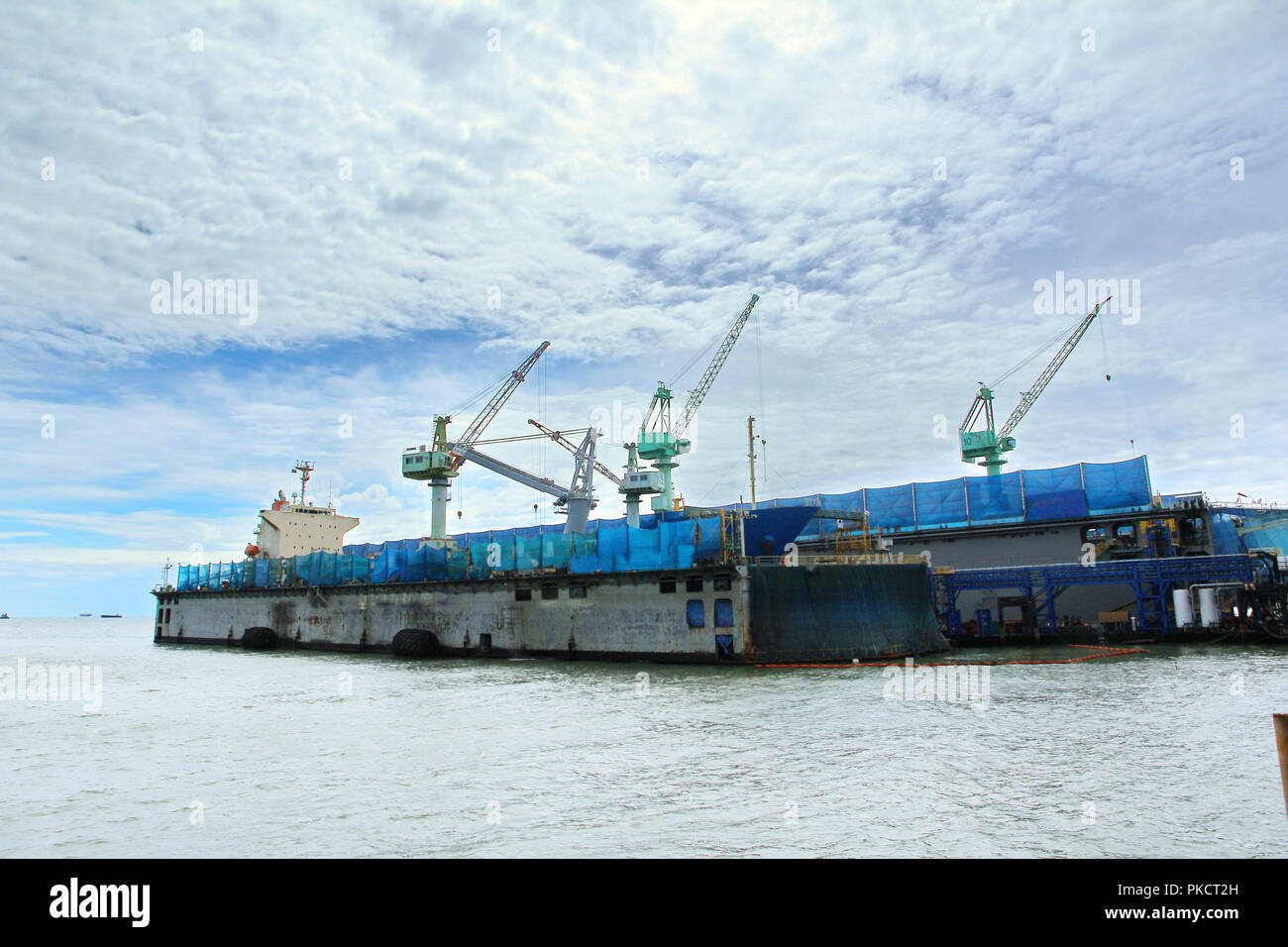Large commercial ships into floating repair dock. The shipyard crane provide blue mesh  fabric  and drop the buoy oil reservoir. To prevent contaminat Stock Photo