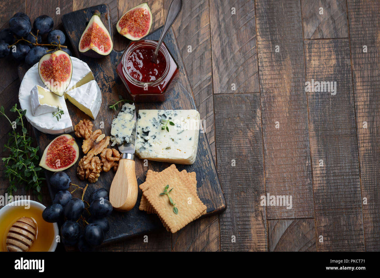 Cheese plate with grapes, figs, crackers, honey, plum jelly, thyme and nuts, selective focus. Stock Photo