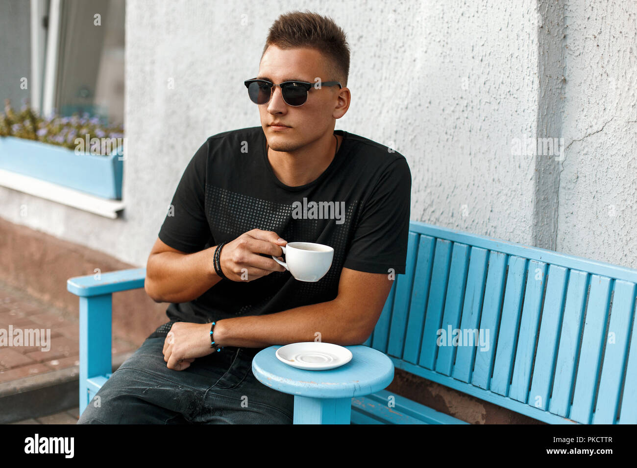 Handsome young man with coffee sitting on a bench. Stock Photo
