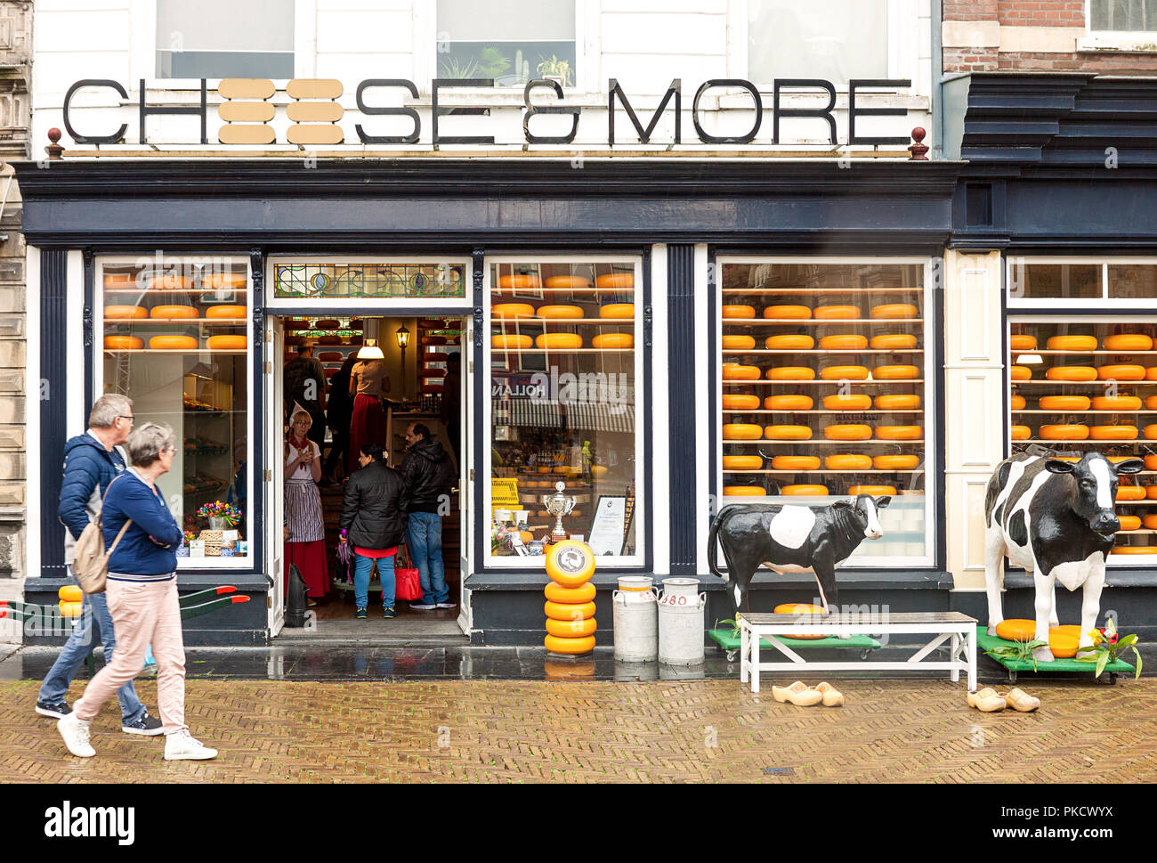 Traditional Dutch cheese and dairy shop entrance with customers inside, tourists passing by and cow moulages in Delft, Netherlands Stock Photo