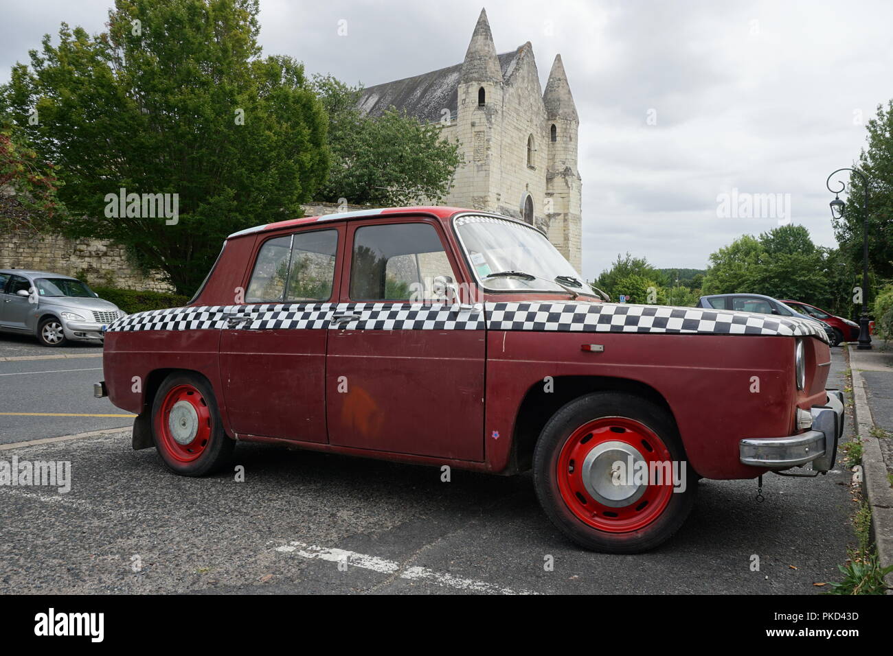 Old vintage red car with black and white checkers paintings parked by an old stone church in a small Loire Valley village Stock Photo