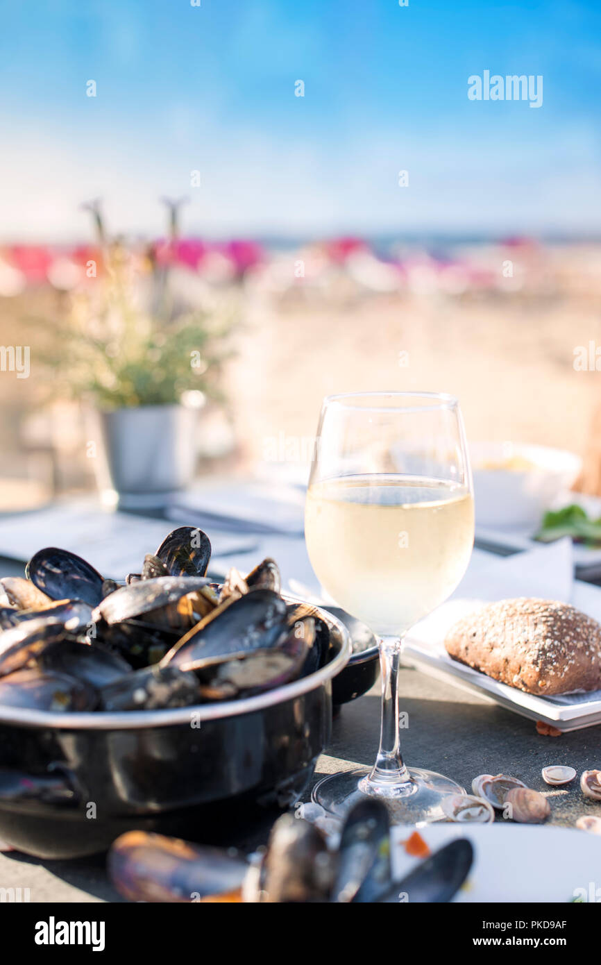 Mussels in a saucepan and a glass of cold white wine. Delicious seafood dinner in a restaurant on the beach. Copy space Stock Photo