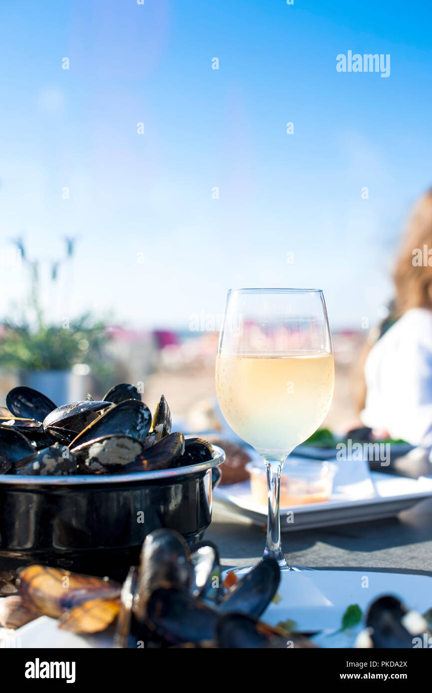 Mussels in a saucepan and a glass of cold white wine. Delicious seafood dinner in a restaurant on the beach. Copy space Stock Photo
