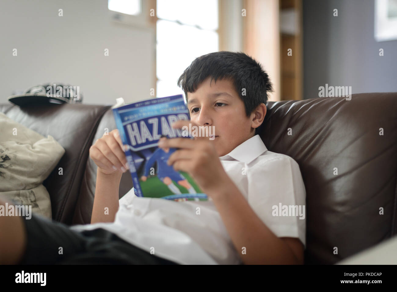 Surrey,UK-Young boy in school uniform  reading football book at home Stock Photo