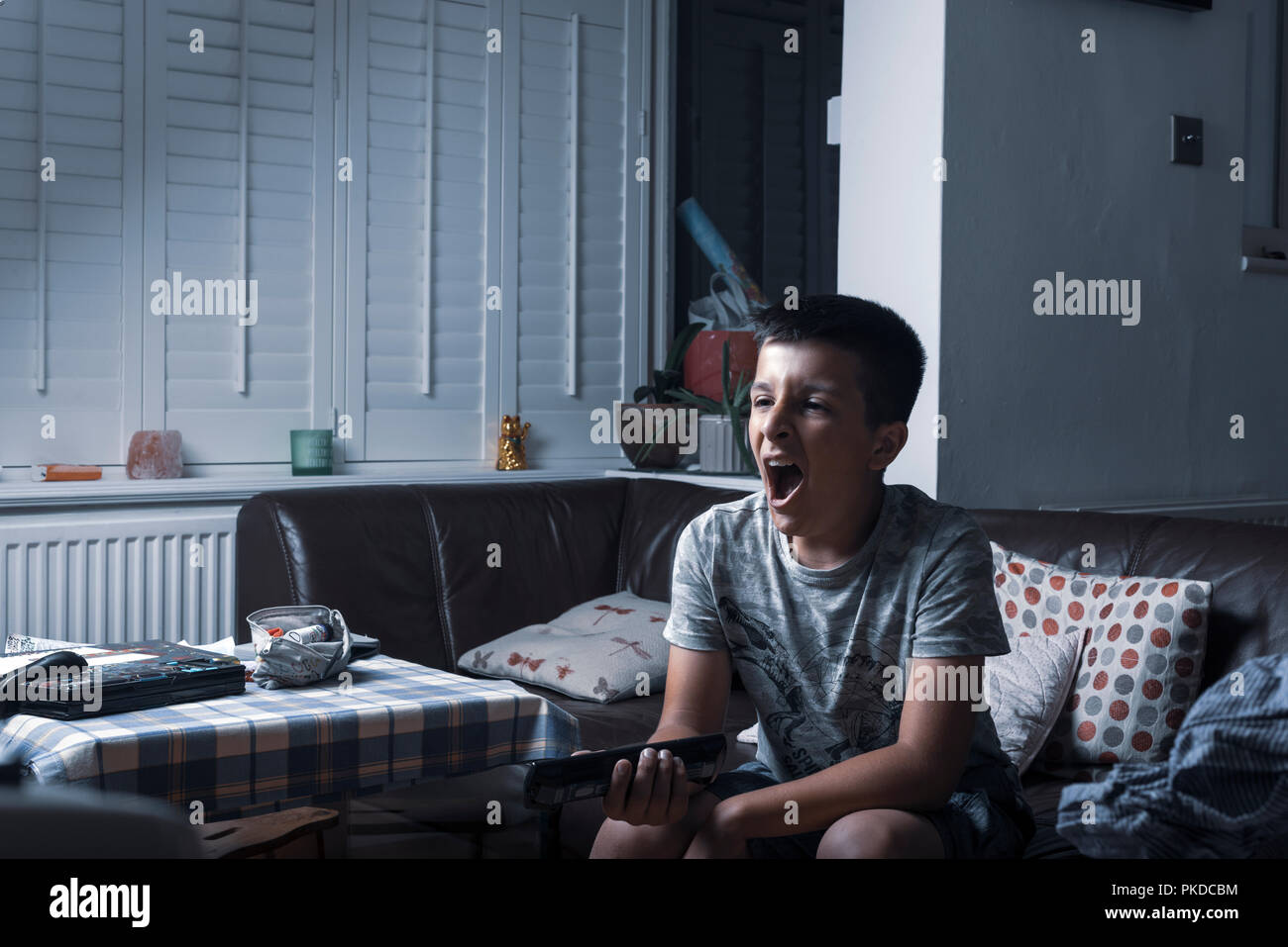Boy watches TV at night- yawns  and holds remote control,UK Stock Photo