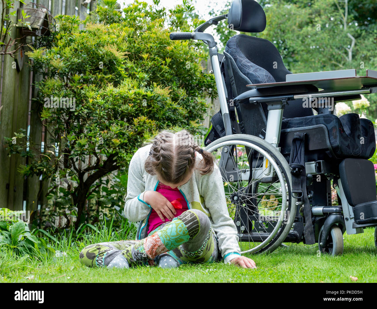 A disabled child having a break from sitting in her wheelchair to explore her natural surroundings Stock Photo