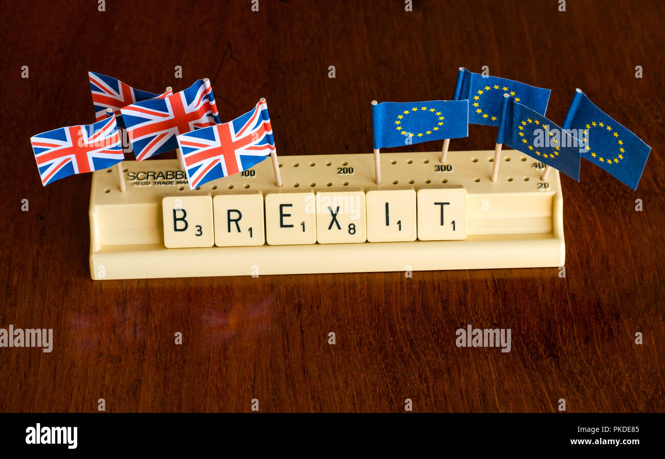 Scrabble letters spelling Brexit in Scrabble tray with British Union Jack and EU flags on dark mahogany background Stock Photo