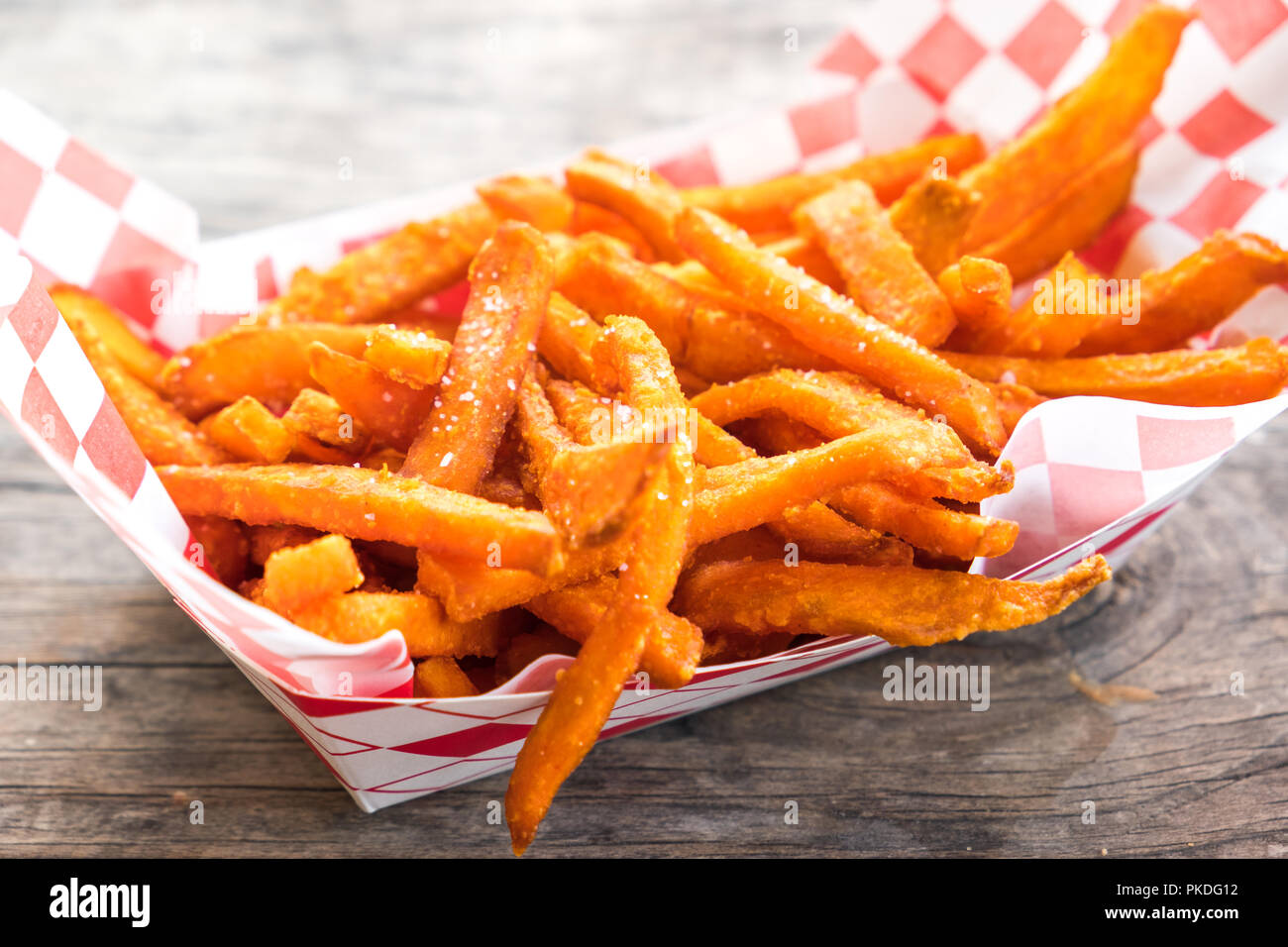 Paper basket of sweet potato fries with salt on rustic wooden table Stock Photo