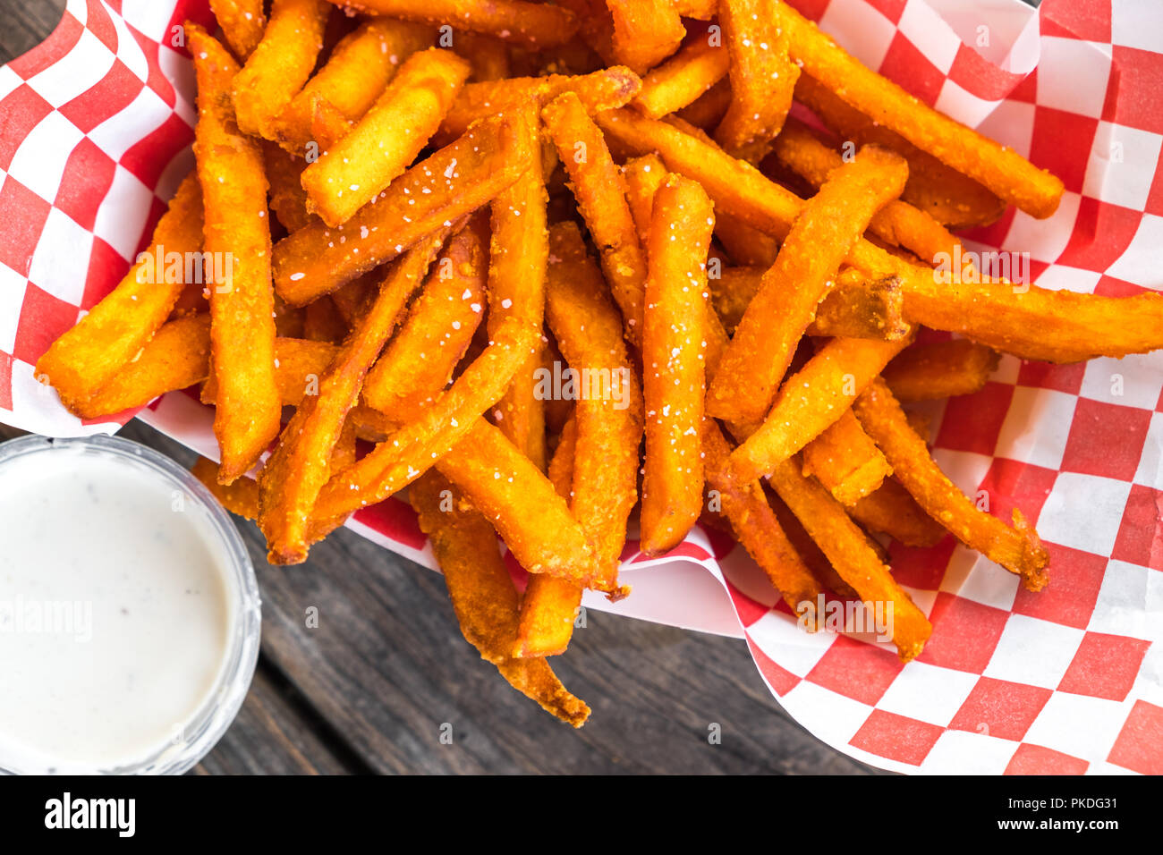 Paper basket of sweet potato fries with salt and a side of ranch dressing on rustic wooden table Stock Photo