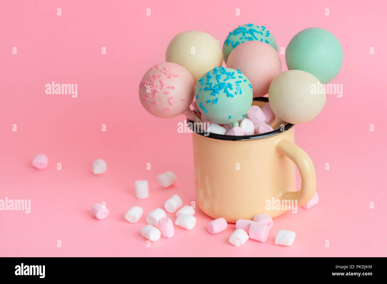 pink, blue, white icing pop cakes and marshmallows in cup over pink background Stock Photo