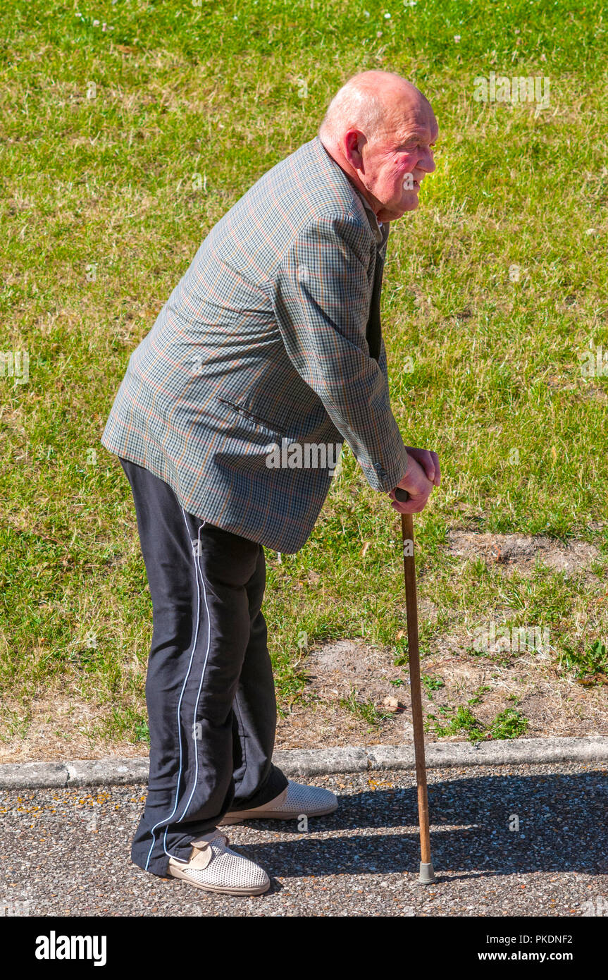 Old man resting on walking stick on pavement - France. Stock Photo