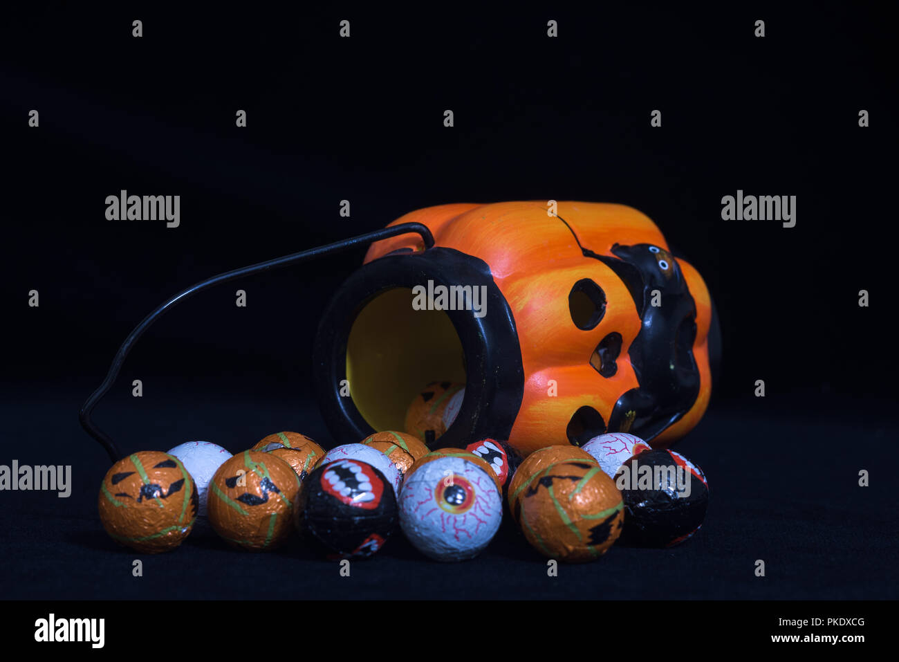 Pumpkin shaped halloween lantern with black cat coming out With lots of round chocolate sweets enclosed in a funny face, on a black background. Useful Stock Photo