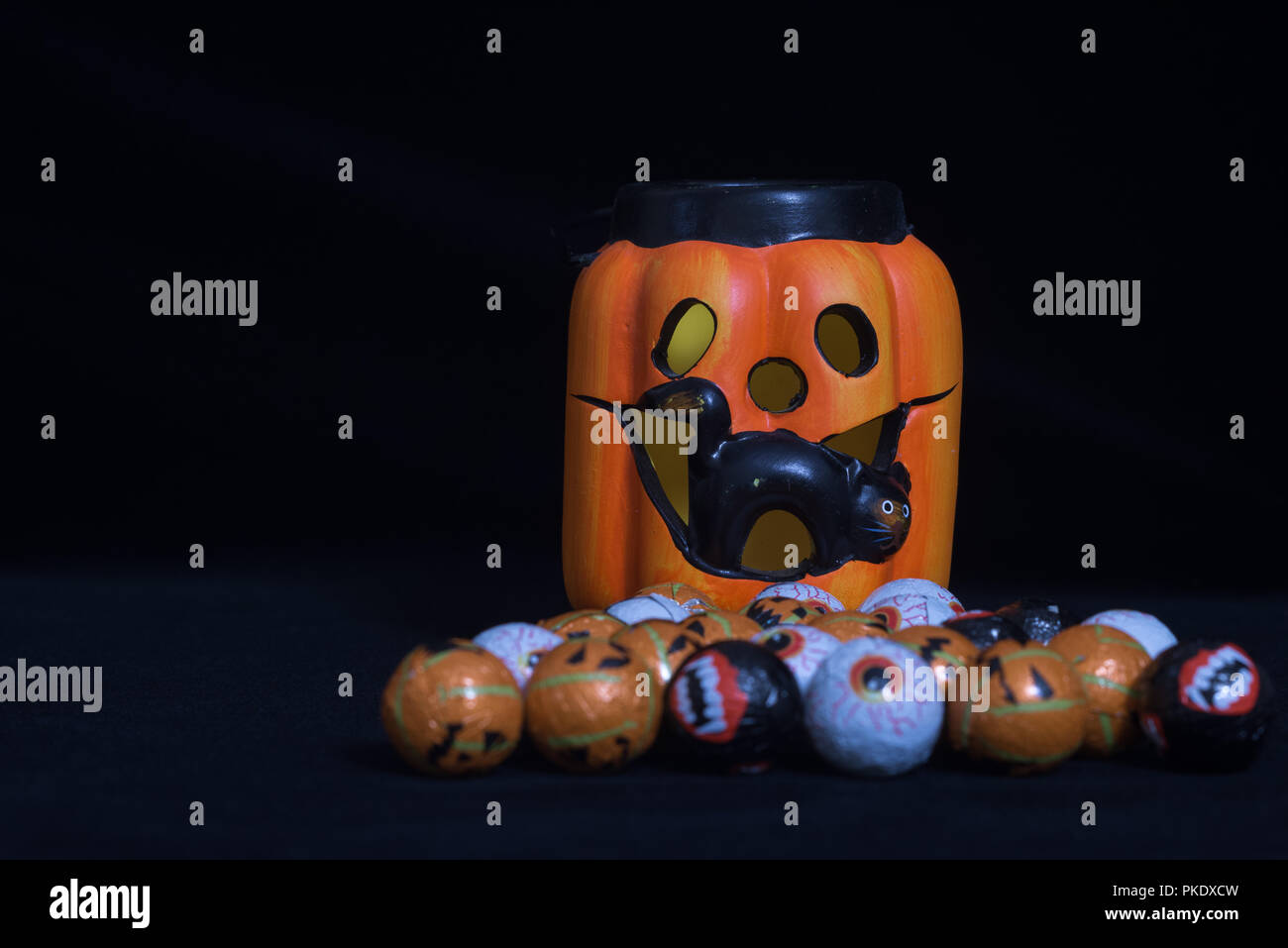 Pumpkin shaped halloween lantern with black cat coming out With lots of round chocolate sweets enclosed in a funny face, on a black background. Useful Stock Photo