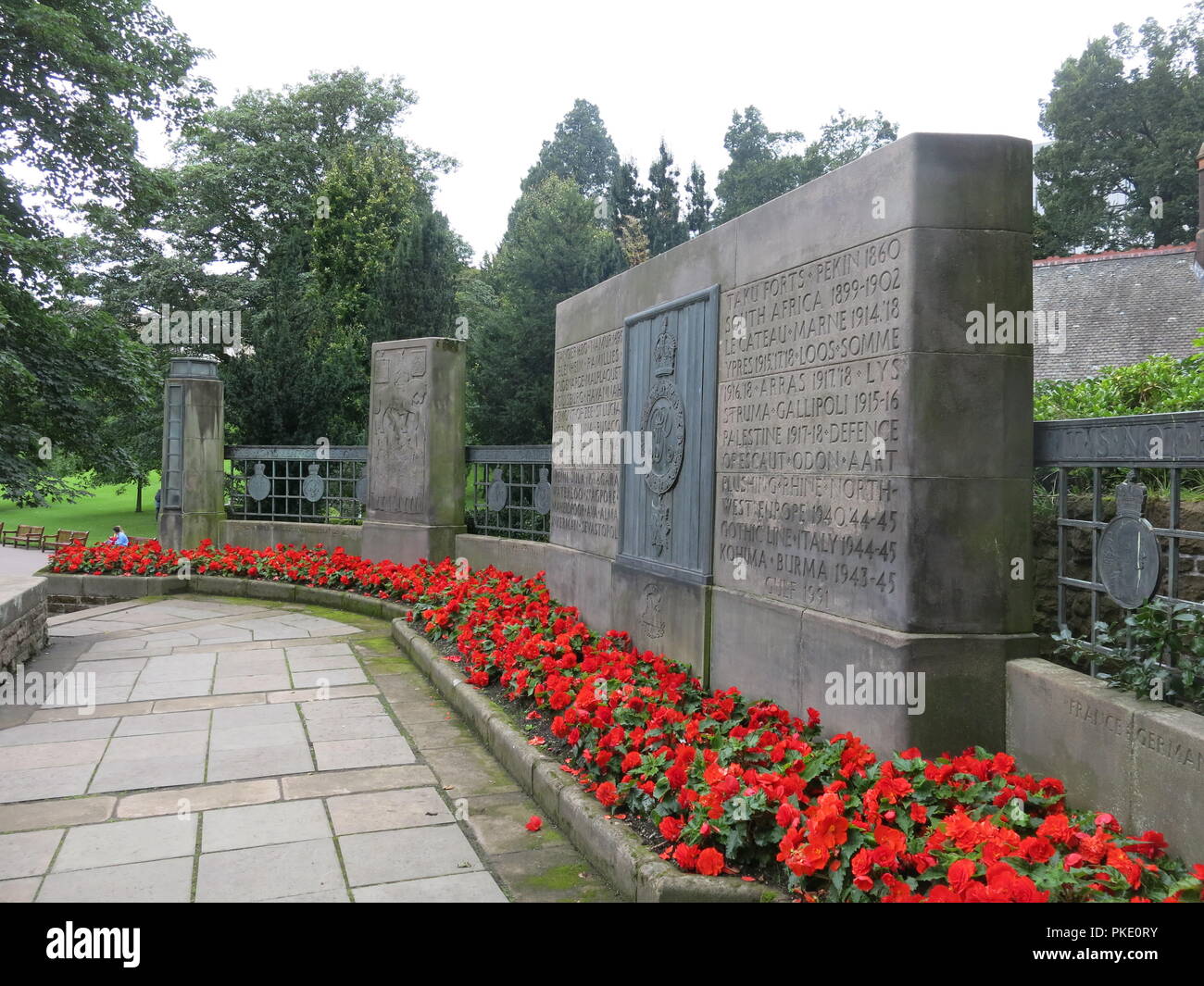 Close-up of a stone monolith & red begonias in the Royal Scots War Memorial inscribed with battles through the ages;  Princes St Gardens, Edinburgh Stock Photo