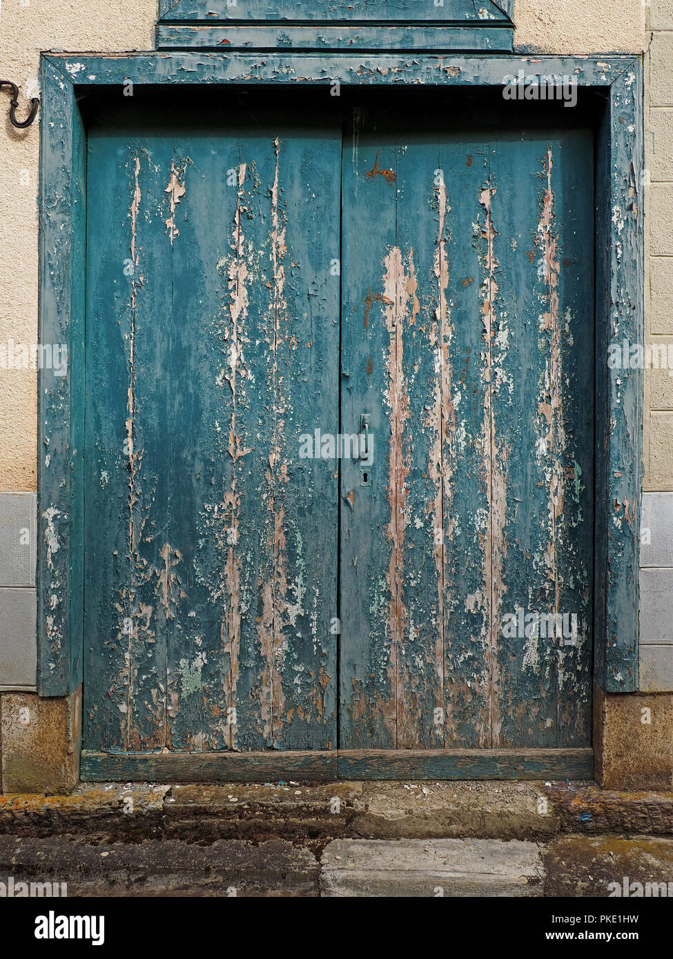 flaking blue paint on rustic wooden double doors of building in the