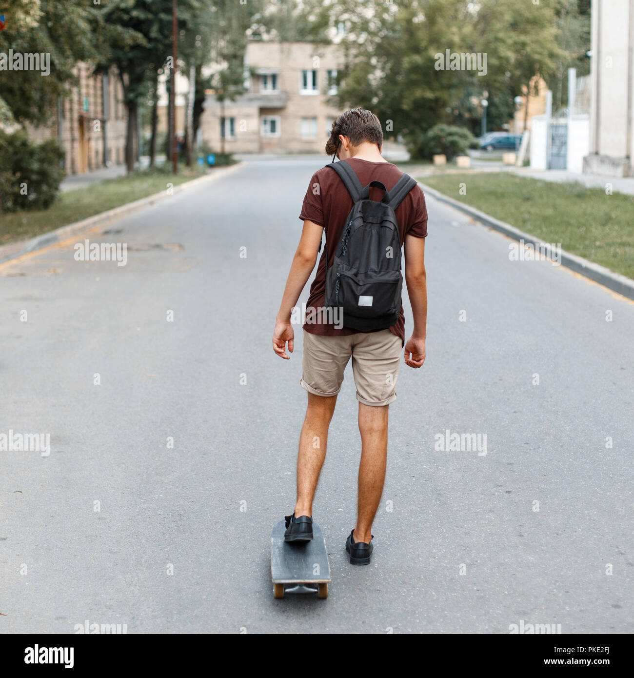 Young handsome guy with a backpack riding a skateboard on the road Stock Photo