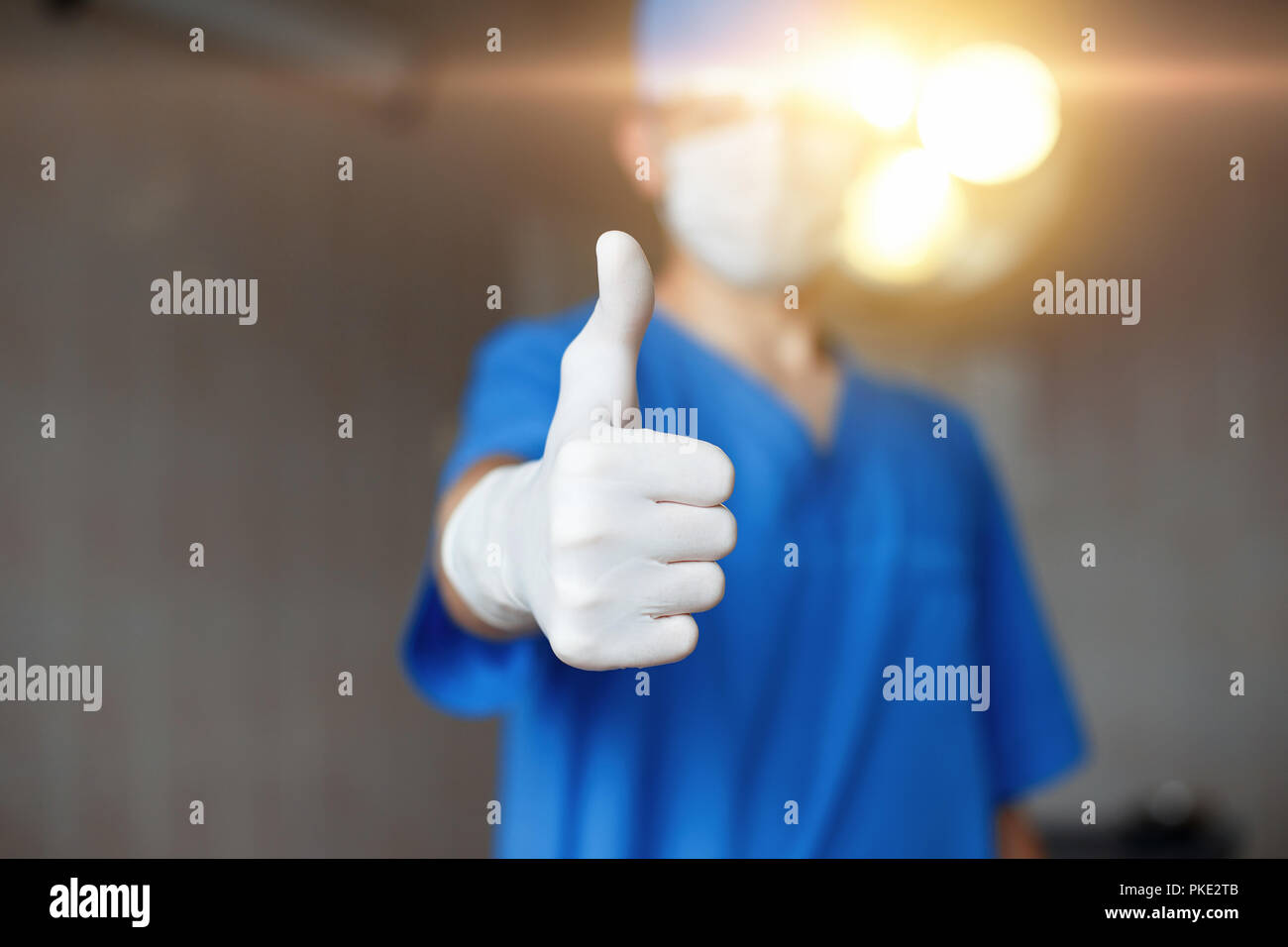 Thumbs up. Doctor in mask and blue costume approves on a background of the operating room. Stock Photo