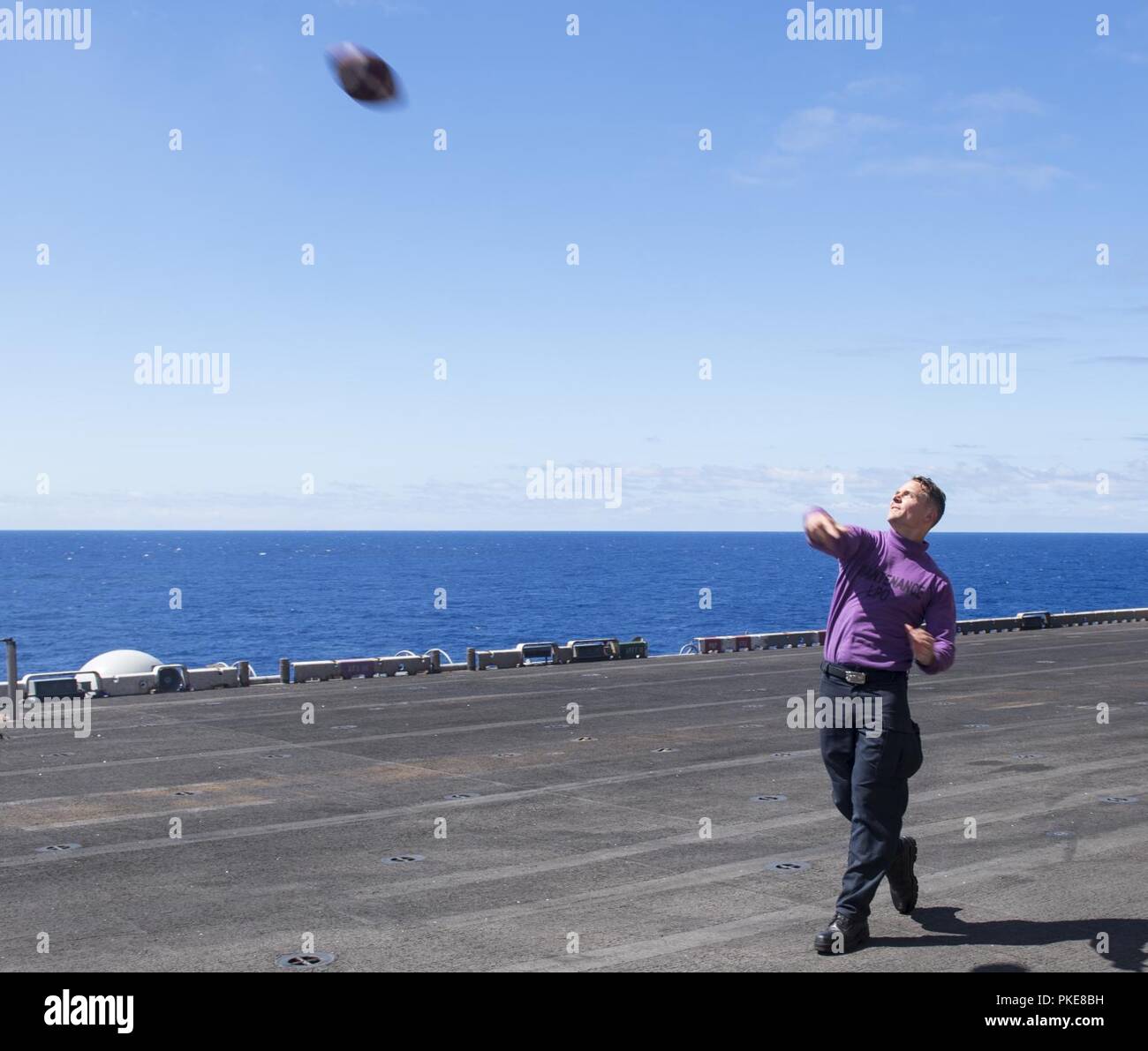 ATLANTIC OCEAN (July 28, 2018) Aviation Boatswain’s Mate (Fuel) 1st Class Jeremy Clautice throws a football on the flight deck during a steel beach picnic aboard the Wasp-class amphibious assault ship USS Iwo Jima (LHD 7) July 28, 2018.  Iwo Jima, homeported in Mayport, Florida, is conducting naval operations in the U.S. 6th Fleet area of operations in support of U.S. national security interests in Europe and Africa. Stock Photo