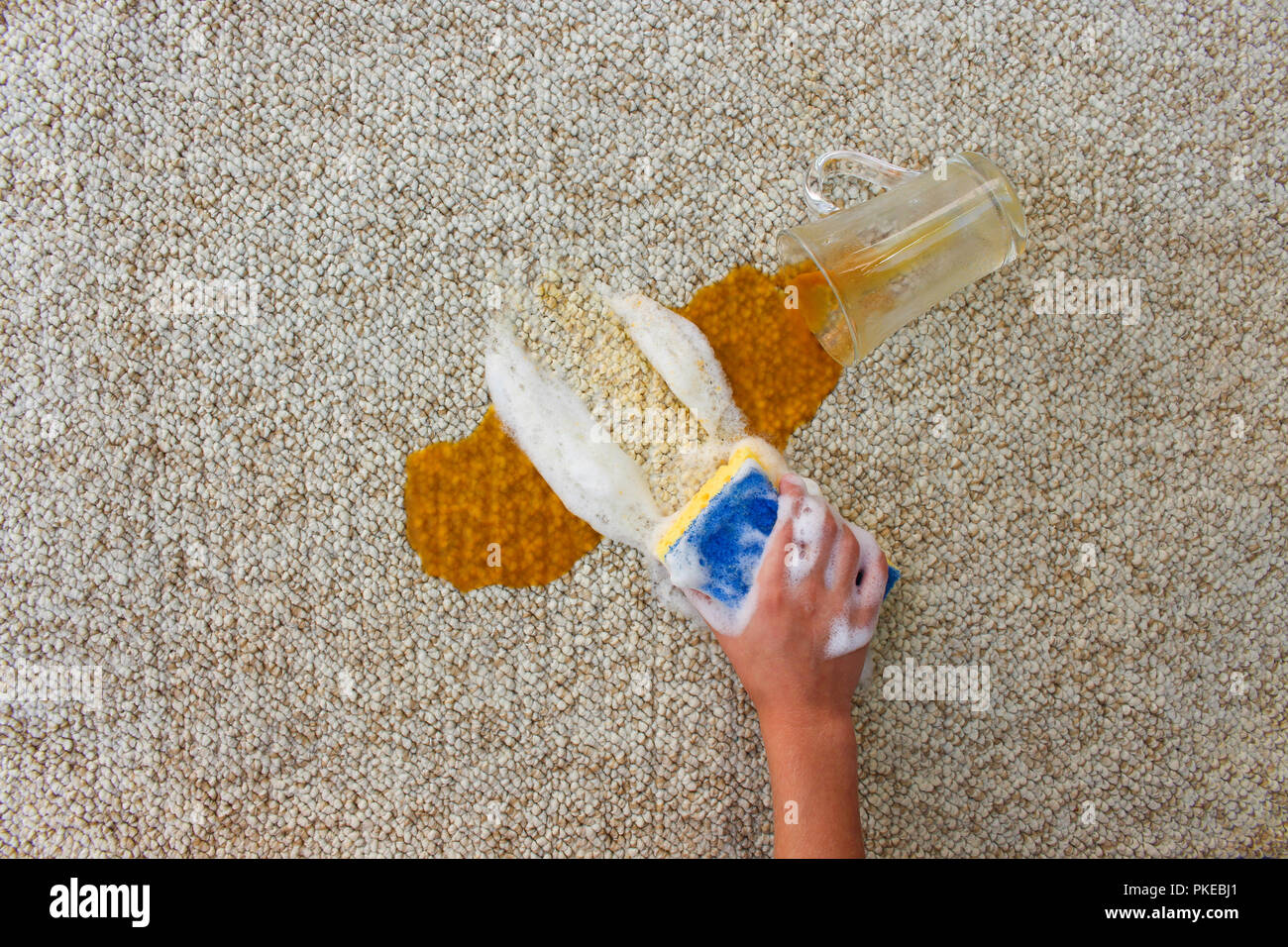 Glass of juice fell and spilled on floor. Female hand cleans the carpet