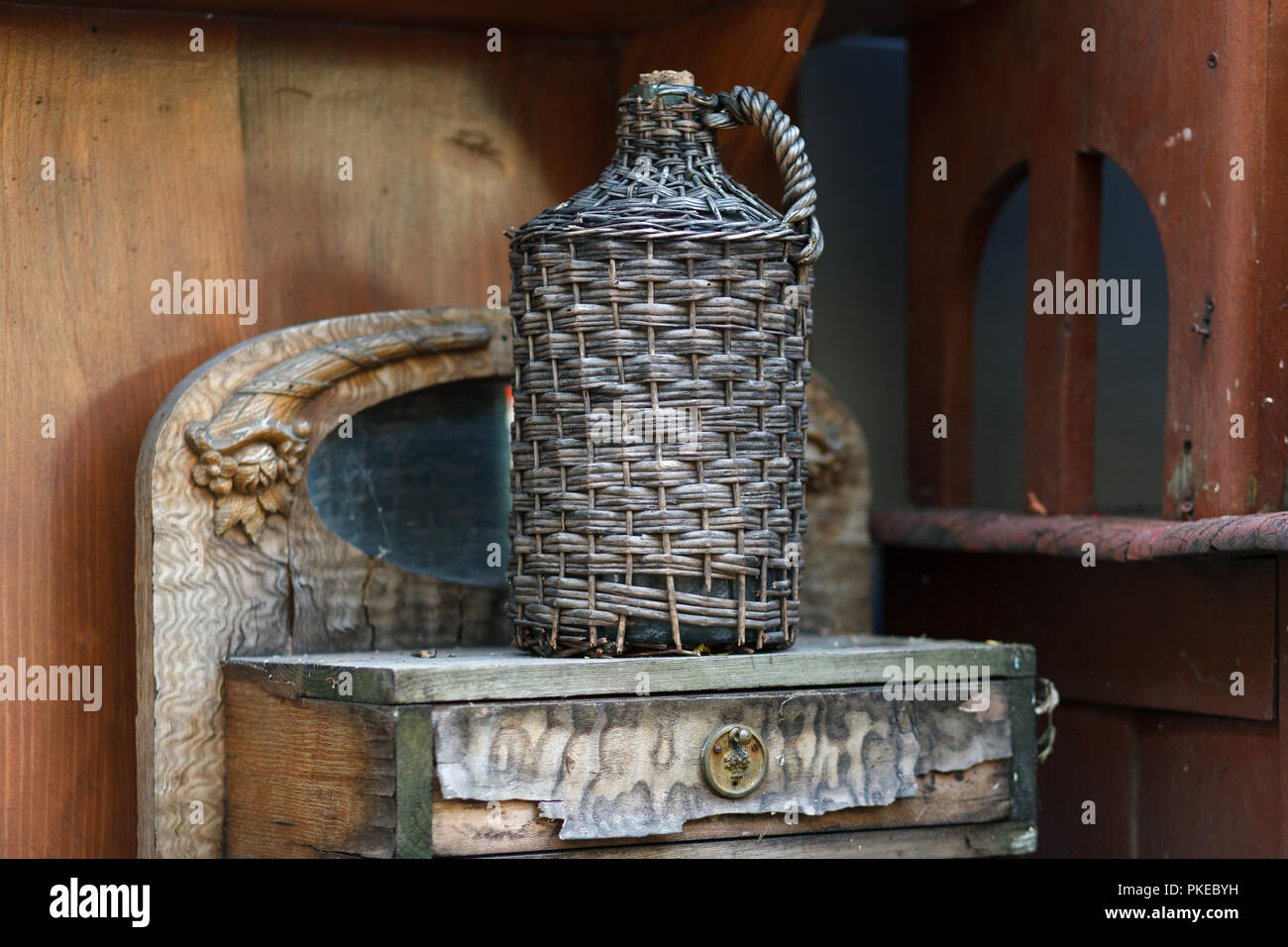 Carboy in wicker basket on wooden table. Old demijohn wicker wrapped