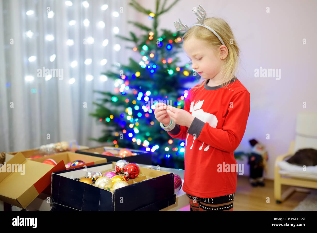 Adorable little girl decorating the Christmas tree with colorful glass