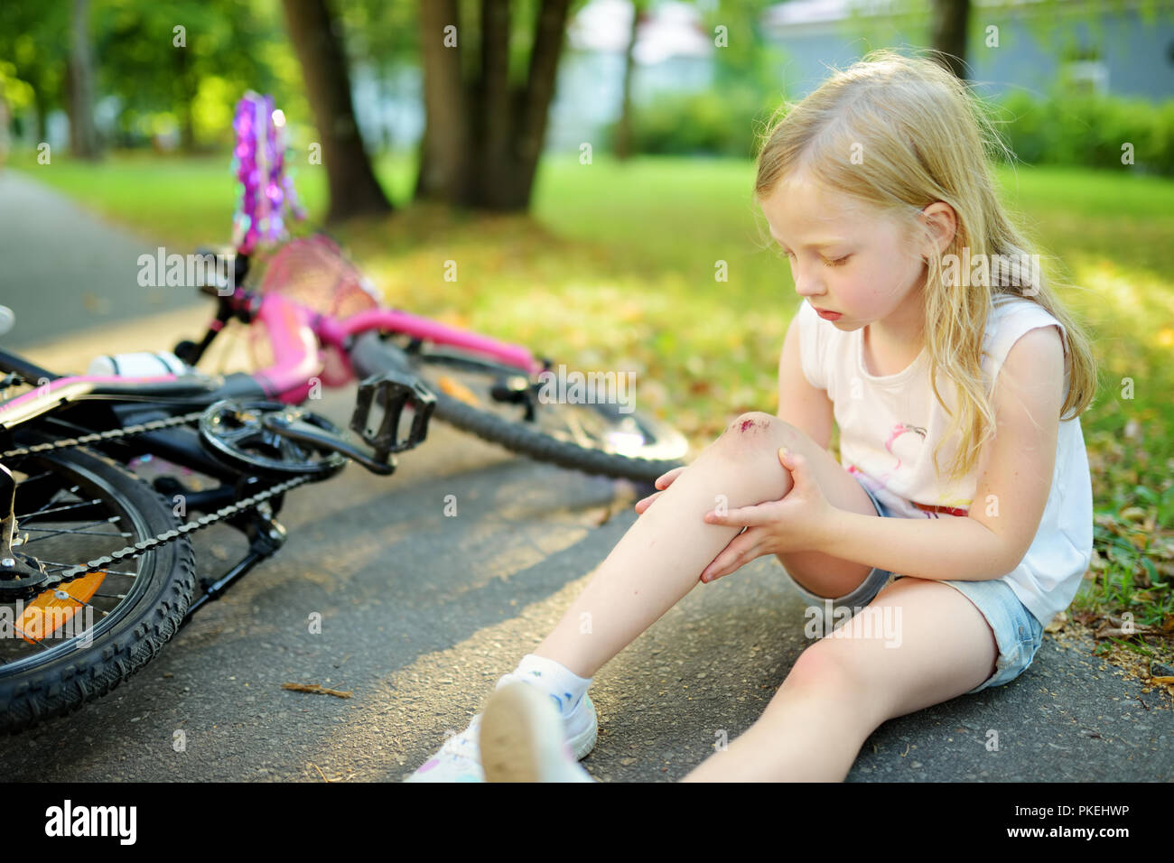 Cute little girl sitting on the ground after falling off her bike at summer park. Child getting hurt while riding a bicycle. Active family leisure wit Stock Photo Alamy