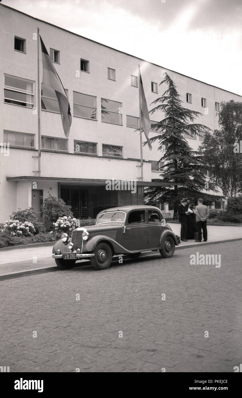 1950s, historical, Koln, Gemany, a Mercedes motorcar with a French numberplate parked on a cobbled steet outside a modern building, possibly an appartment block, with a nun and two men on the pavement looking at a map and having a discussion. Stock Photo