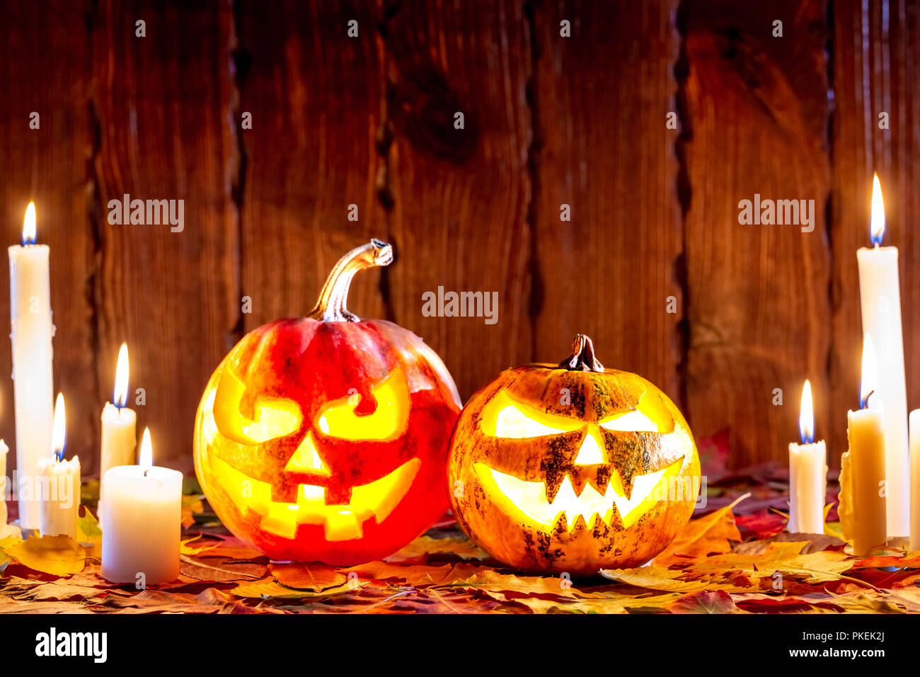 Halloween pumpkin with glowing face on a wooden background with many flaming candles and autumn leaves. Idea for flyers, poster, placard, billboard Stock Photo
