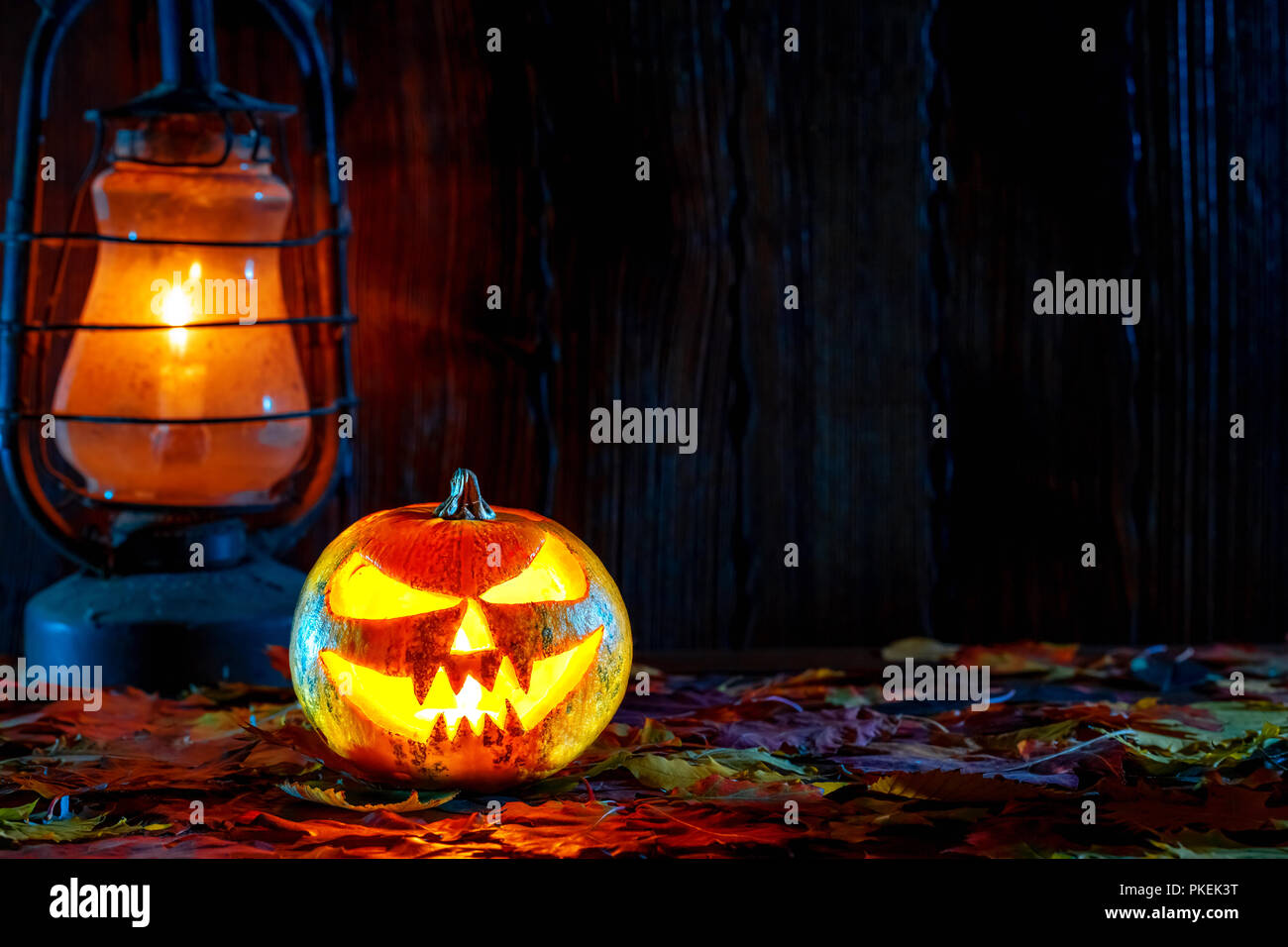 Halloween pumpkin with glowing face on a wooden background with candles. Stock Photo