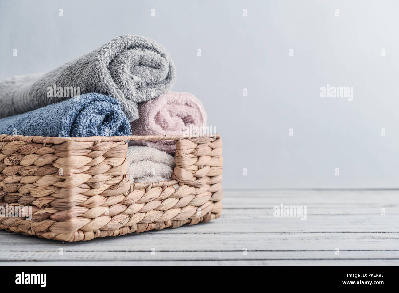 Bath towels of different colors in wicker basket on light background
