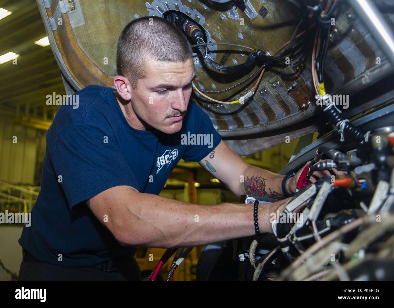 PACIFIC OCEAN (July 30, 2018) – Aviation Electronics Technician 3rd Class Ryan Baker, assigned to the “Blackjacks” of Helicopter Sea Combat Squadron (HSC) 21, conducts maintenance on an MH-60S Seahawk helicopter in the hangar bay of Wasp-class amphibious assault ship USS Essex (LHD 2) during a regularly scheduled deployment of the Essex Amphibious Ready Group (ARG) and 13th Expeditionary Unit (MEU). The Essex ARG/13th MEU is a capable and lethal Navy-Marine Corps team deployed to the 7th fleet area of operations to support regional stability, reassure partners and allies and maintain a presenc Stock Photo