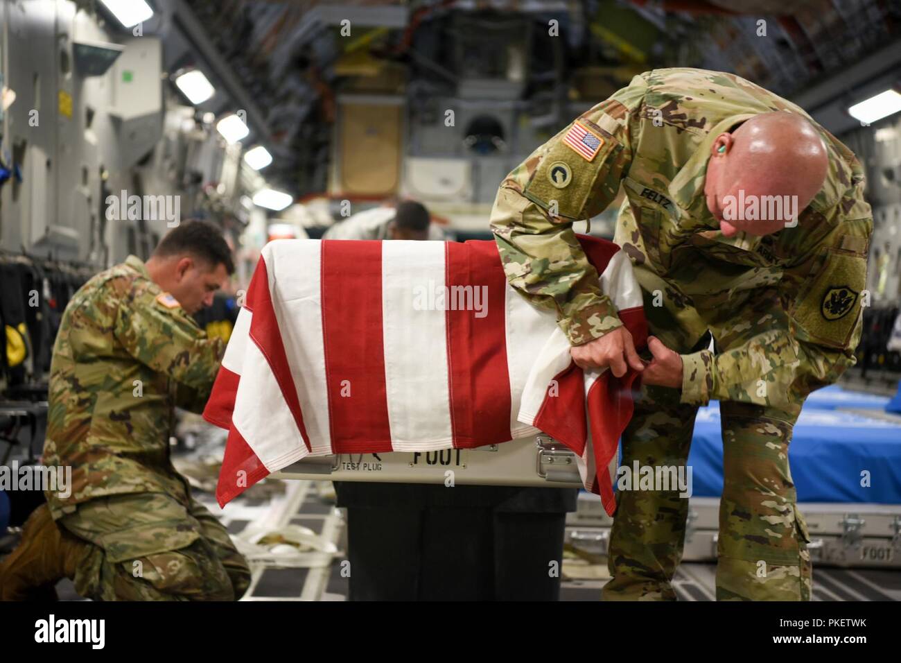 U.S. Army Staff Sgt. Marc Weyrick, left, and Sgt. 1st Class Eric Feltz, mortuary affairs specialists assigned to the Defense POW/MIA Accounting Agency (DPAA), secure a U.S. flag onto a transfer case aboard an Air Force C-17 Globemaster III en route to Joint Base Pearl Harbor-Hickam, Hawaii, from Osan Air Base, Republic of Korea, Aug. 1, 2018. The cases contain possible remains of service members lost during the Korean War and were transferred to DPAA's forensic laboratory in Hawaii to begin the identification process in support of the agency's mission to provide the fullest possible accounting Stock Photo