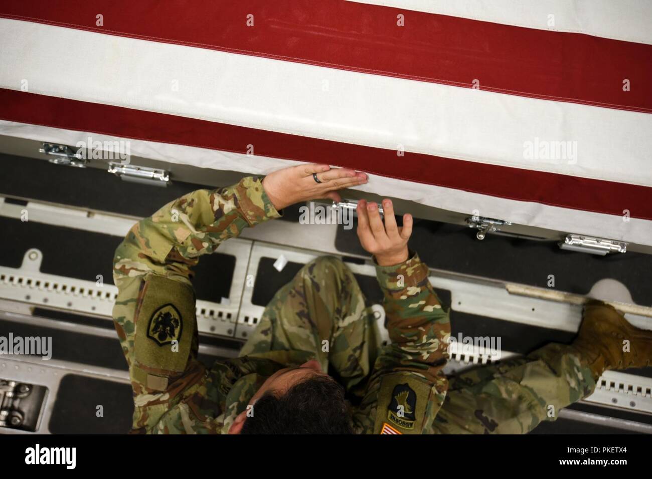 U.S. Army Staff Sgt. Marc Weyrick, mortuary affairs specialist assigned to the Defense POW/MIA Accounting Agency (DPAA), secures a U.S. flag onto a transfer case aboard an Air Force C-17 Globemaster III en route to Joint Base Pearl Harbor-Hickam, Hawaii, from Osan Air Base, Republic of Korea, Aug. 1, 2018. The cases contain possible remains of service members lost during the Korean War and were transferred to DPAA's forensic laboratory in Hawaii to begin the identification process in support of the agency's mission to provide the fullest possible accounting of our missing to their families and Stock Photo