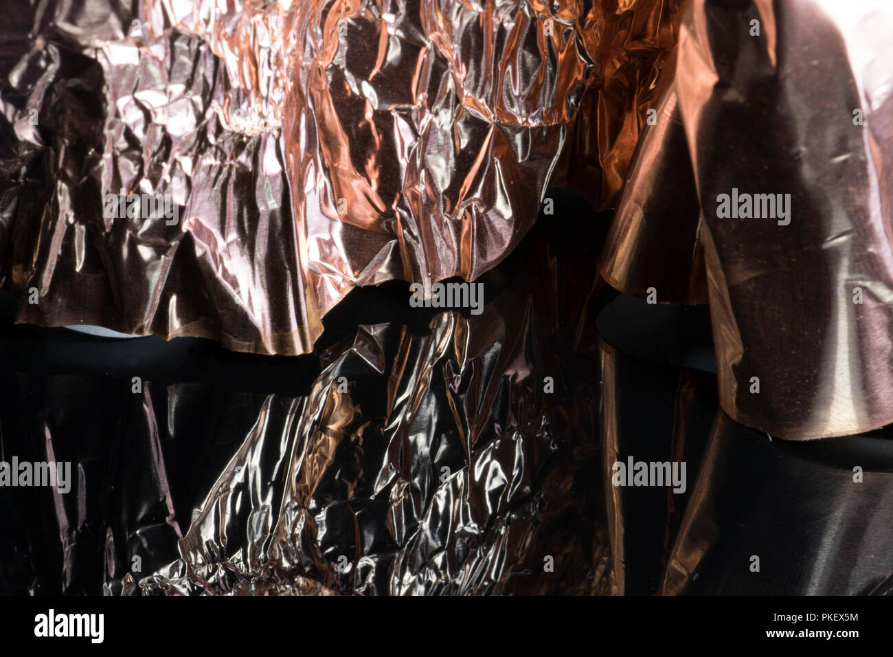 https://c8.alamy.com/comp/PKEX5M/crushed-shiny-metallic-gold-bronze-tin-foil-reflecting-on-a-black-shiny-surface-crumpled-sheet-of-uneven-foil-PKEX5M.jpg