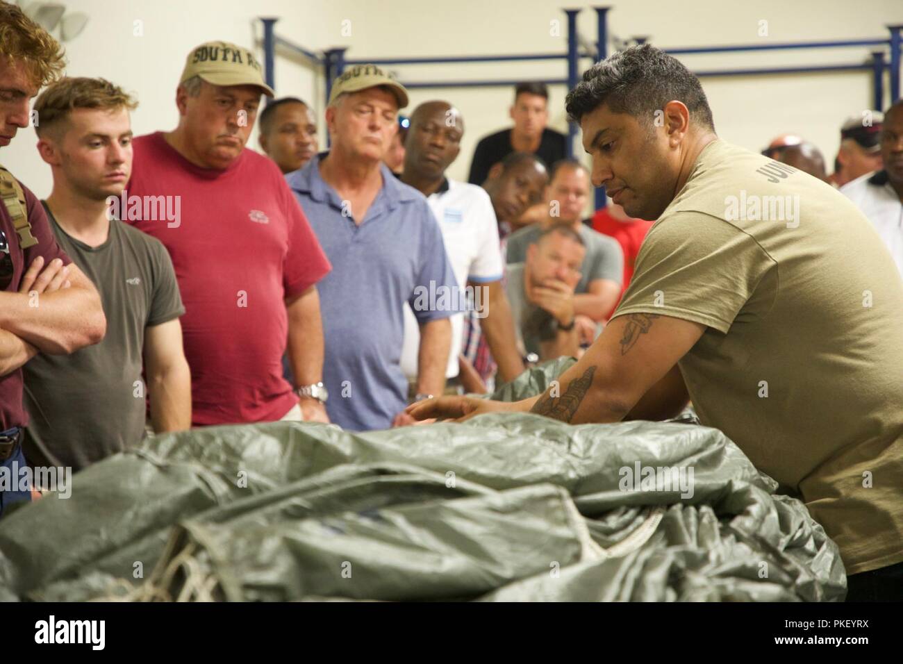 U.S. Army Sgt. Roger Montanez, assigned to Rigger Detachment, 56th Troop Command, teaches a group of International Paratroopers how to pack a MC-6 parachute at Building 216, Parachute Rigger Facility Shed, during Leapfest 2018 at West Kingston, RI., August 3, 2018. Leapfest is the largest, longest standing, international static line parachute training event and competition hosted by the 56th Troop Command, Rhode Island Army National Guard to promote high level technical training and esprit de corps within the International Airborne community. Stock Photo