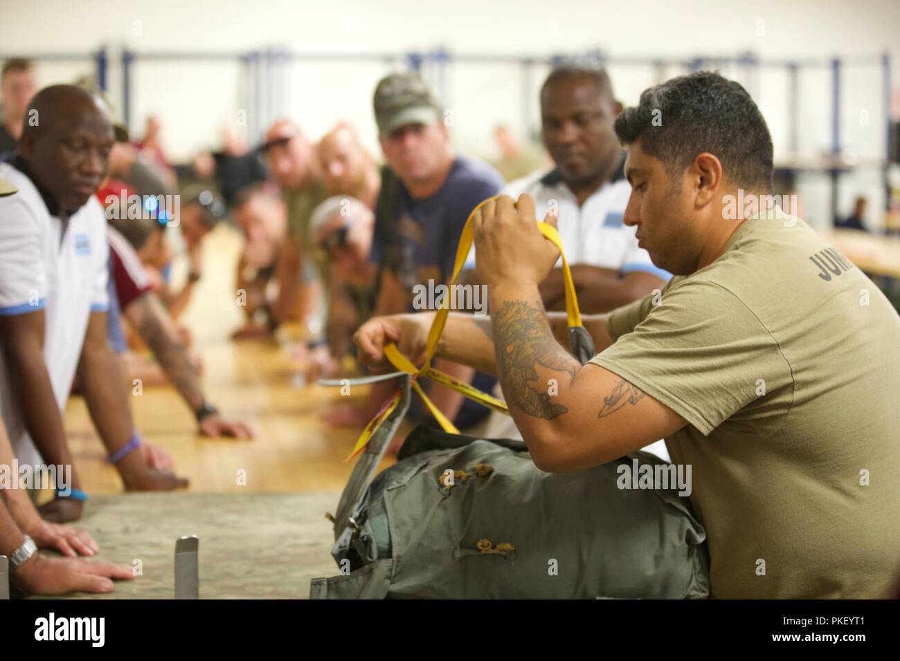U.S. Army Sgt. Roger Montanez, assigned to Rigger Detachment, 56th Troop Command, teaches a group of International Paratroopers how to pack a MC-6 parachute at Building 216, Parachute Rigger Facility Shed, during Leapfest 2018 at West Kingston, RI., August 3, 2018. Leapfest is the largest, longest standing, international static line parachute training event and competition hosted by the 56th Troop Command, Rhode Island Army National Guard to promote high level technical training and esprit de corps within the International Airborne community. Stock Photo