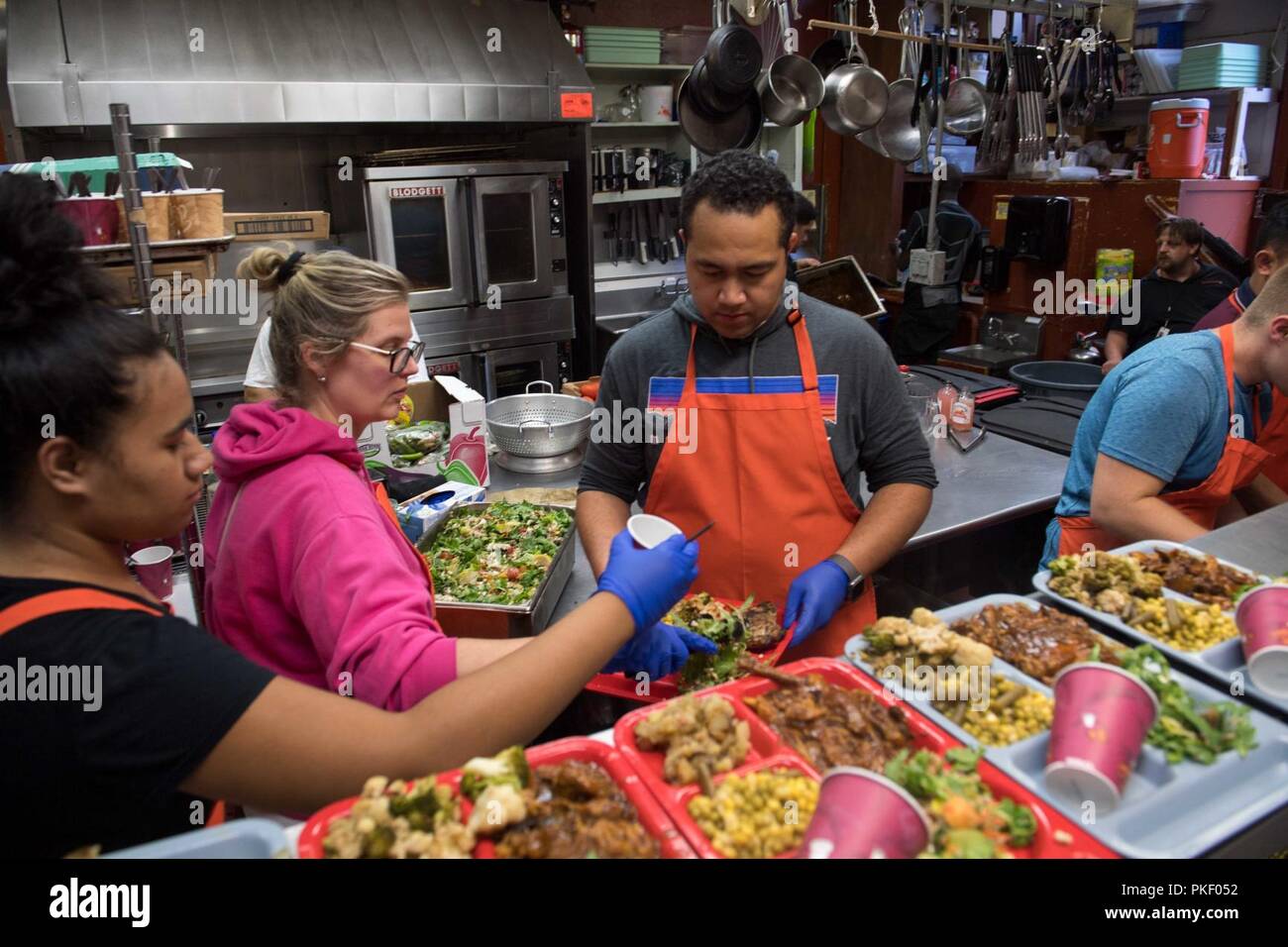 SEATTLE (Aug. 3, 2018) Hospital Corpsman 1st Class Jonathan Faletoi (right), assigned to Naval Hospital Bremerton, prepares meals with his wife, Stephanie, (middle), and sister, Patricia, (left), at Bread of Life Mission during a Seattle Seafair Fleet Week community relations event. Seafair Fleet Week is an annual celebration of the sea services wherein Sailors, Marines and Coast Guard members from visiting U.S. Navy and Coast Guard ships and ships from Canada make the city a port of call. Stock Photo