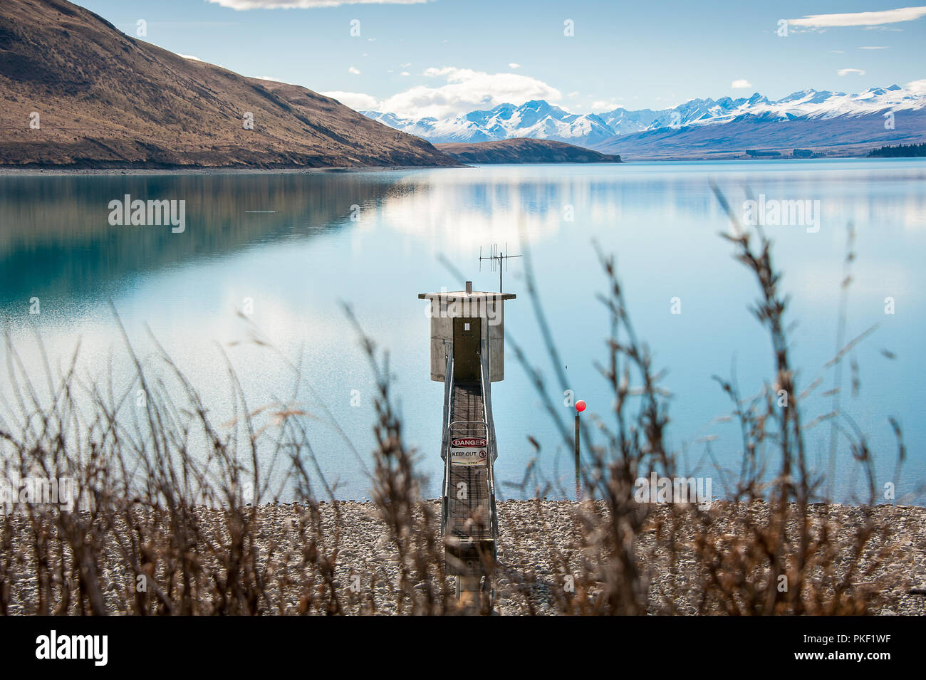 Lake Tekapo, New Zealand. Shoreline with small electrical substation, turquoise lake and view to snow covered Southern Alps in the background. Stock Photo