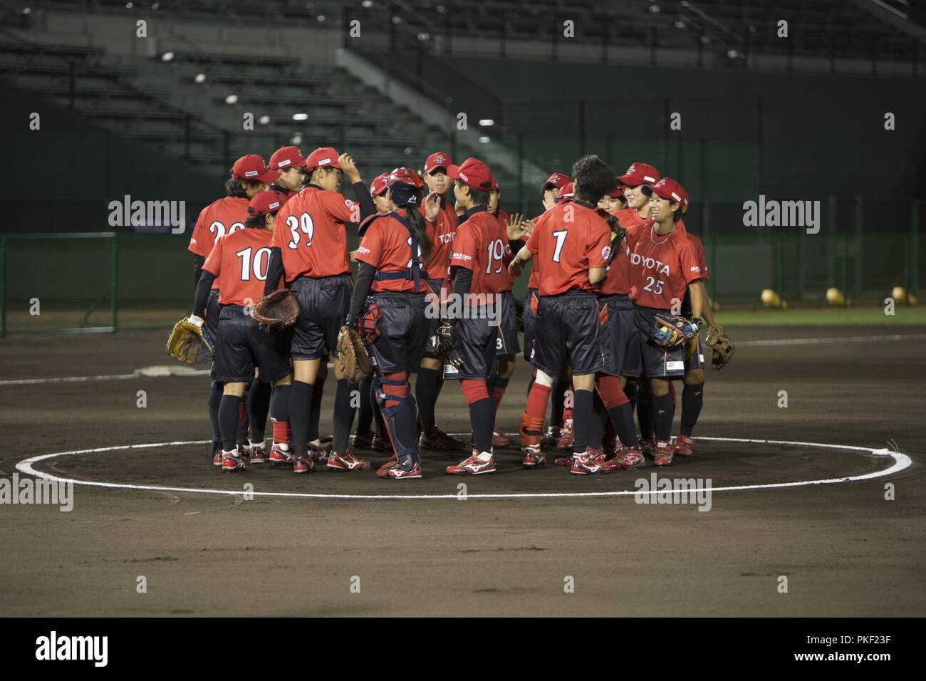 Members of the Japanese Toyota Red Terriers softball team stand on a pitcher’s mound during a