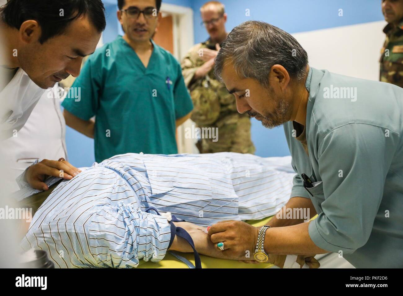 KANDAHAR PROVINCE, Afghanistan (August 5, 2018) -- Afghan radiology technicians prepare a patient for a body scan, August 5, 2018, after receiving advice from U.S. Navy Lt. Cdr. Justin S. Clark, radiology technician for Kandahar Airfield NATO Role III Multinational Medical Unit, during a medical advisory visit at Kandahar Regional Military Hospital, Camp Hero in Kandahar, Afghanistan. Staff members from the Role III conduct routine visits to KRMH to train and advice Afghan medical staff. Stock Photo