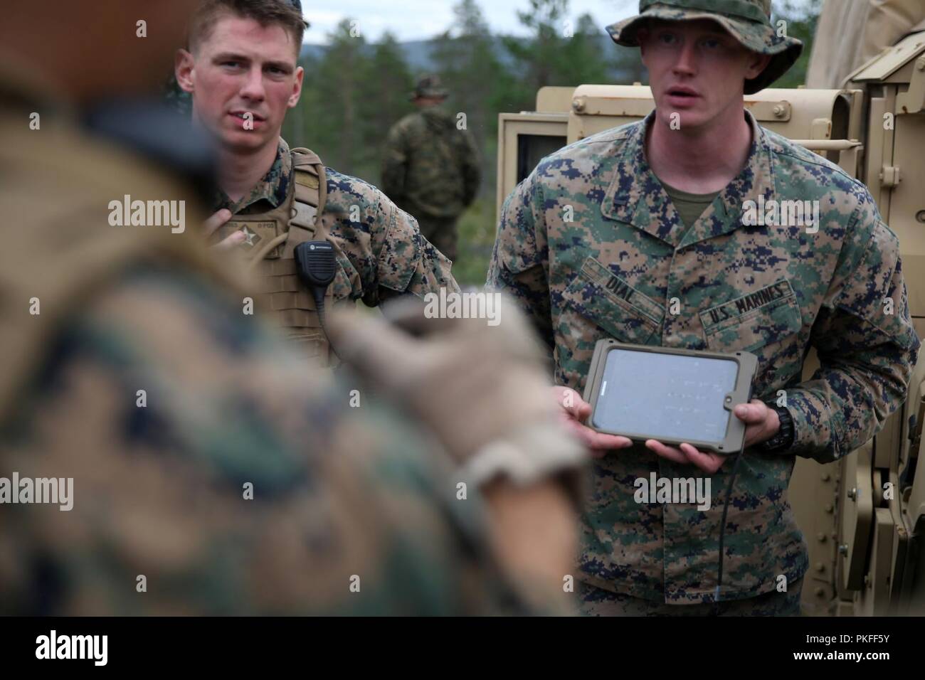 A U.S. Marine with Marine Rotational Force-Europe 18.1 gives a brief about the Marine Air Ground Task Force (MAGTF) Common Handheld during a platoon-supported attack range at Giskas, Norway, Aug. 7, 2018. The MCH enables Marines to relay messages and locations to other users in a manner similar to text messaging.  The tablet’s capabilities will augment previous methods of radio contact, allowing quieter and more efficient long-distance communication. Stock Photo