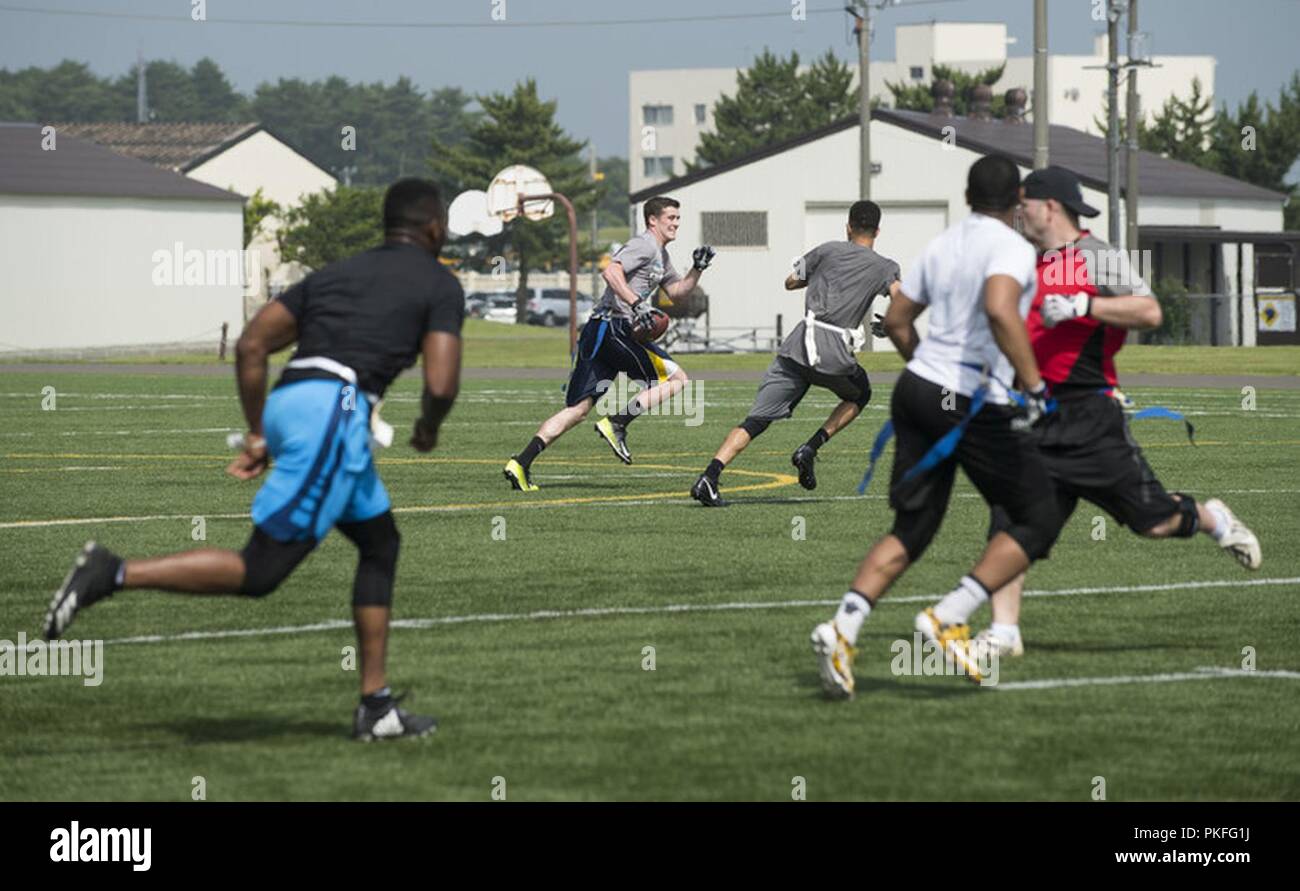 U.S. Air Force Airman 1st Class Kevin Cheeseman, center, a 35th Medical Operations Squadron aerospace medical technician, runs the ball during a game of flag football at Misawa Air Base, Japan, July 27, 2018. Flag football was one of 16 events that took place during the second annual Team Misawa Resilient Relationships and Appreciation Day. Stock Photo