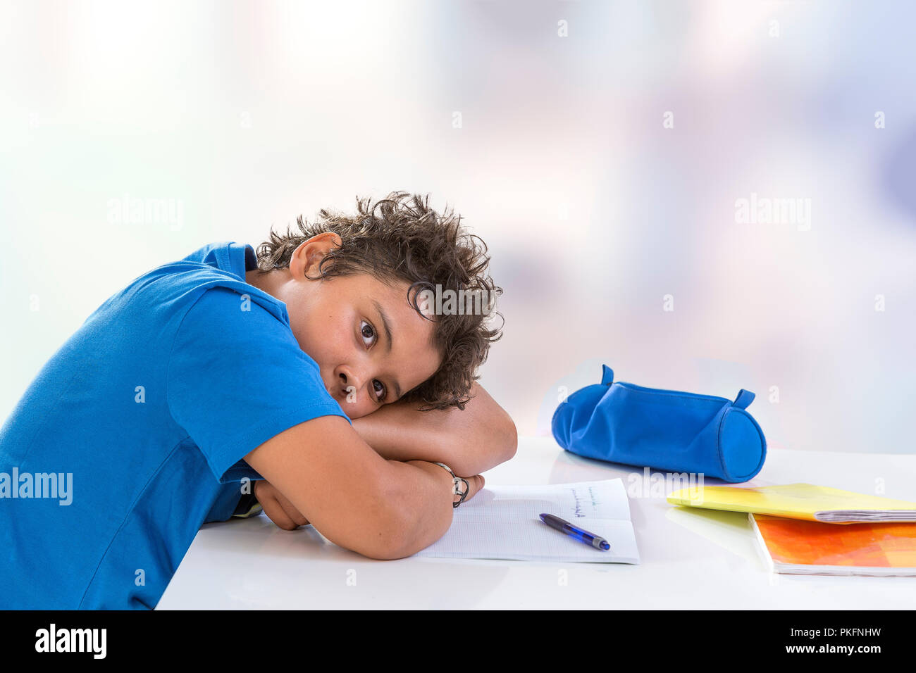 Overwhelmed schoolboy. Bored and tired teenage boy doing homework on desk in his room,seems sleepinp Stock Photo