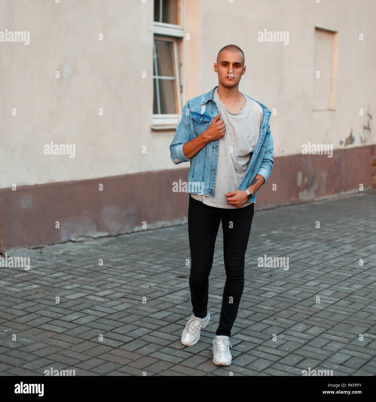 Stylish young man in a denim jacket, a gray T-shirt and black jeans in white shoes on the street Stock Photo